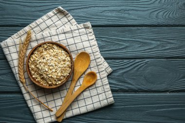 Bir kase çiğ yulaf ezmesi, kaşık ve dikenler koyu ahşap arka planda.