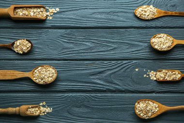 Koyu ahşap arka planda çiğ yulaf ezmeli kaşıklar ve kepçeler.