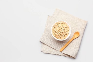 Beyaz arka planda bir kase çiğ yulaf ezmesi ve kaşık