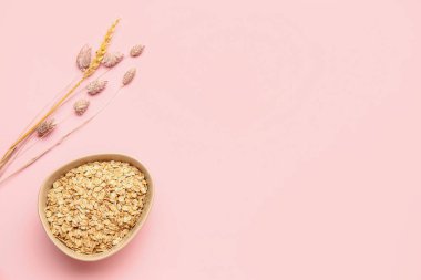 Bir kase çiğ yulaf ezmesi ve pembe arka planda kurumuş çiçekler.