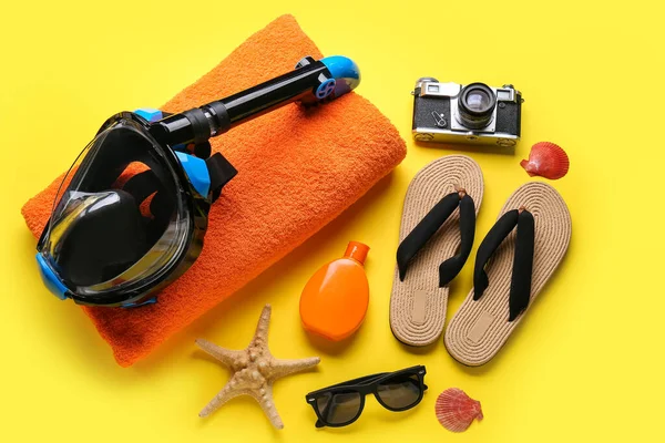 Dalış maskeli plaj aksesuarları, deniz kabukları ve sarı arka planda fotoğraf makinesi.