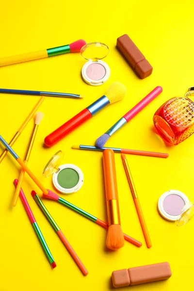 Sarı zemin üzerinde makyaj fırçaları ve kozmetik ürünleri olan kompozisyon