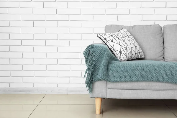 Yastıklı ve ekoseli modern kanepe odada tuğla duvarın yanında.