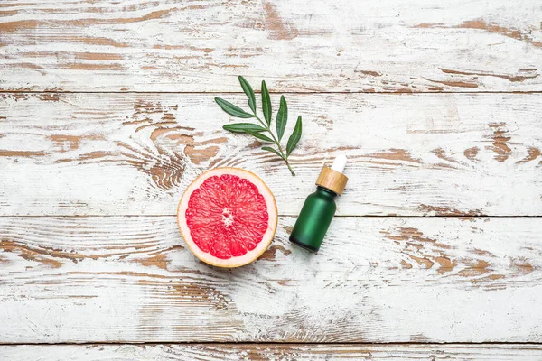 Hafif ahşap zemin üzerinde greyfurt ve gerekli yağ şişesinin yarısıyla kompozisyon