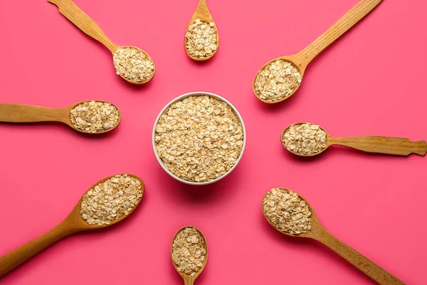 Pembe arka planda çiğ yulaf ezmeli kase ve kaşıklar.