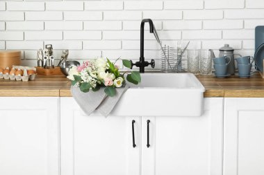 Güzel çiçeklerle lavabo ve mutfak gereçleri beyaz tuğla duvarın yanındaki tezgahlarda.