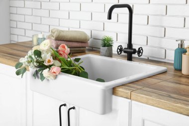 Güzel çiçeklerle lavabo ve banyo malzemeleri beyaz tuğla duvarın yanındaki tezgahlarda.