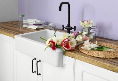 Güzel çiçeklerle lavabo ve mutfak aletleri leylak duvarın yanındaki tezgahlarda.