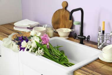 Seramik lavabo güzel çiçekler ve mutfak gereçleri leylak duvarın yanındaki tezgahlarda.