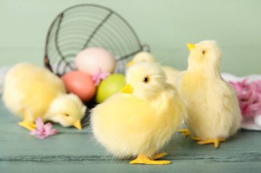 Sevimli tavuklar, ters çevrilmiş sepet. Paskalya yumurtaları ve tahta masanın üzerinde çiçekler.