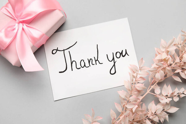 Лист бумаги с текстом СПАСИБО, подарочная коробка и ветвь растений на сером фоне