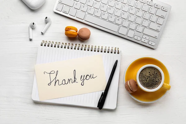 Teşekkürler yazılı defter, kurabiyeler, kulaklıklar, bilgisayar klavyesi ve beyaz ahşap arka planda bir fincan kahve.