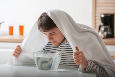 Genç adam burun deliklerini rahatlatmak ve açmak için evde buhar solunumu yapıyor.