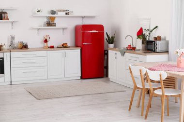 Kırmızı buzdolabı, tezgah ve yemek masası olan açık mutfak.