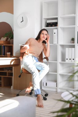 Genç ve çıplak ayaklı bir kadın ofiste oturuyor.