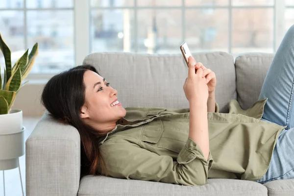 Cep telefonuyla evdeki kanepede uzanan güzel bir Asyalı kadın.