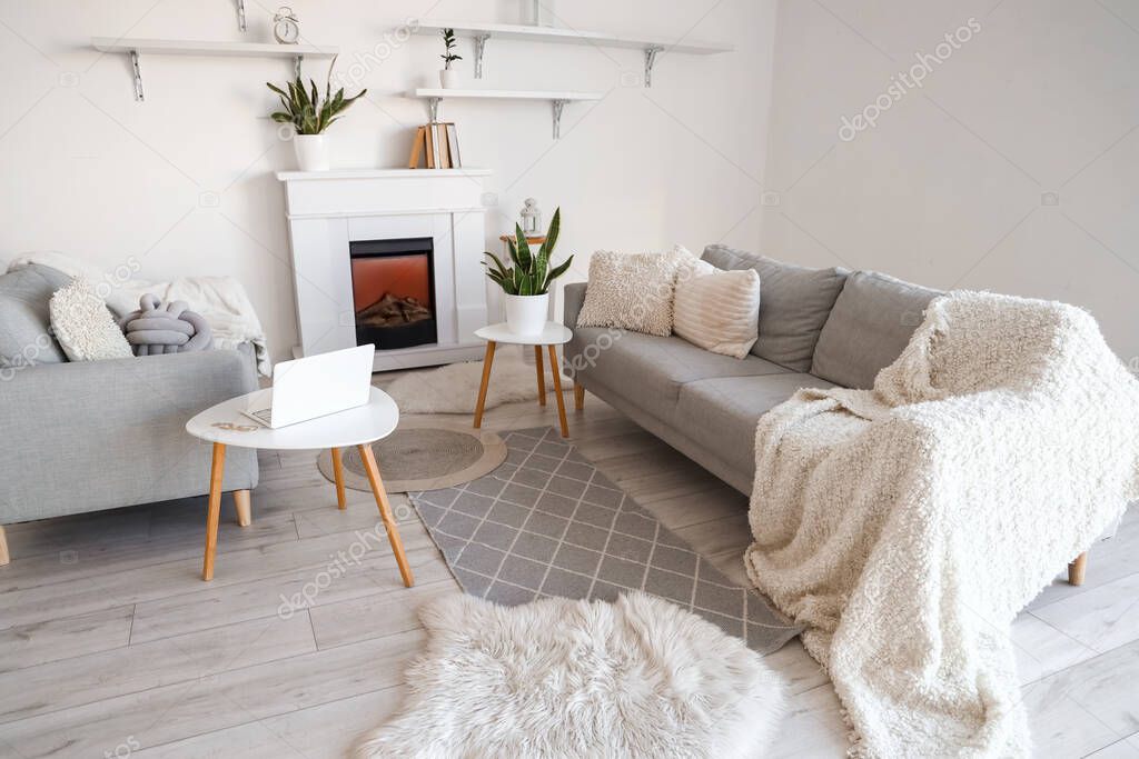 Interior of stylish room with sofas, modern laptop and fireplace near white wall