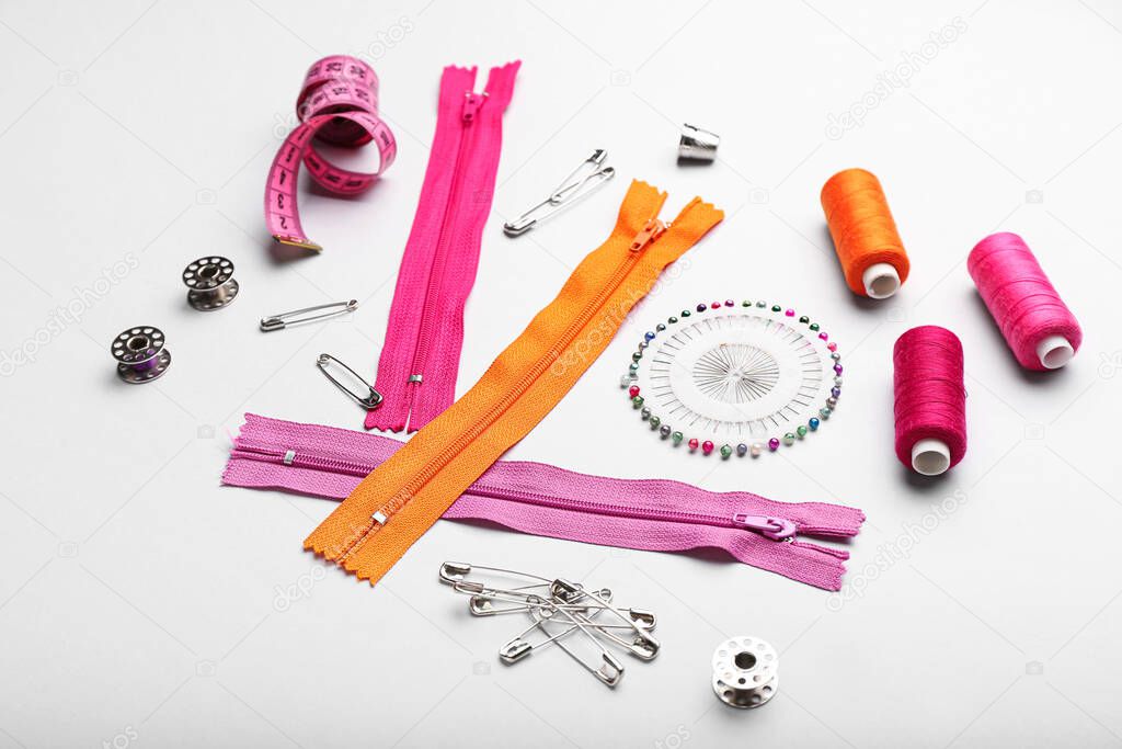 Set of colorful zippers and sewing supplies on light background