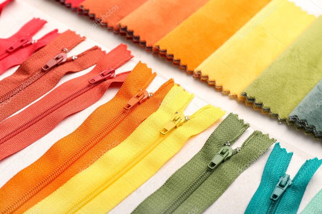 Stylish different zippers and fabric samples on light background