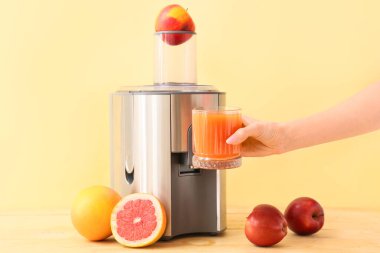 Kadın eli, elinde taze meyve suyu bardağı ve masada yeni bir meyve sıkacağı tutuyor.