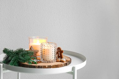 Holders with burning candles, fir branch and cookies on table