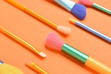 Turuncu arkaplanda renkli makyaj fırçaları, yakın plan.