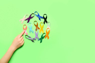 Yeşil arka planda farklı farkındalık kurdeleleri olan kadın eli. Dünya Kanser Günü