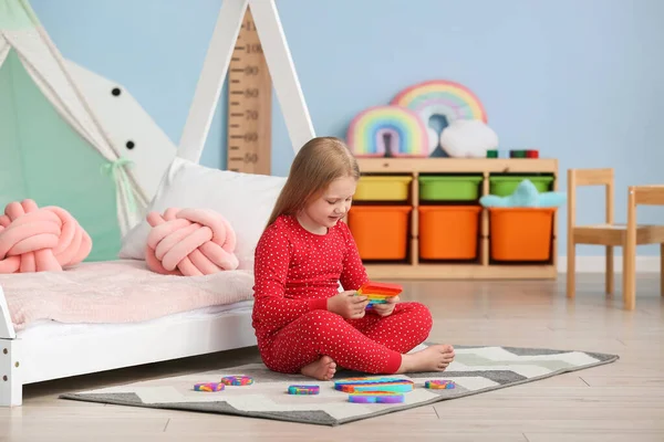 Güzel kız yatağın yanında oturuyor ve çocuk odasında şekerle oynuyor.