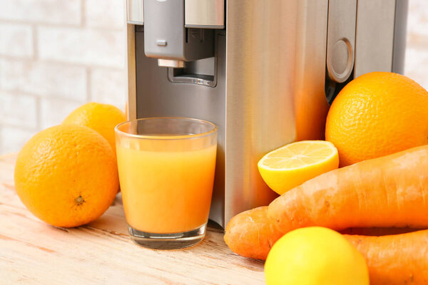 New modern juicer and glass of fresh juice on light wooden table, closeup