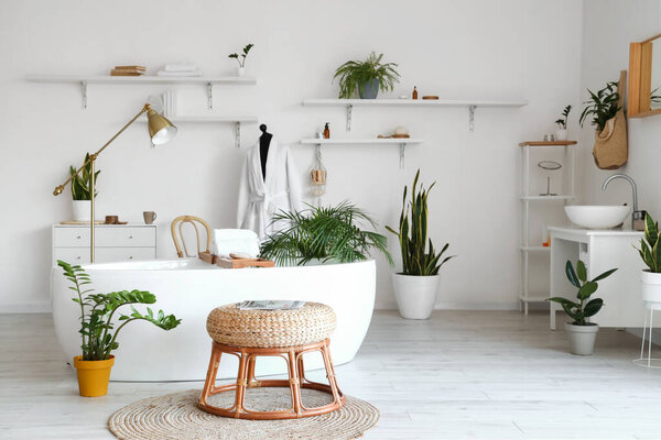 Interior of light bathroom with bathtub, mannequin and houseplants