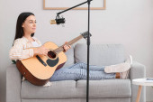 Krásná žena s profesionálním mikrofonem hraje doma na kytaru