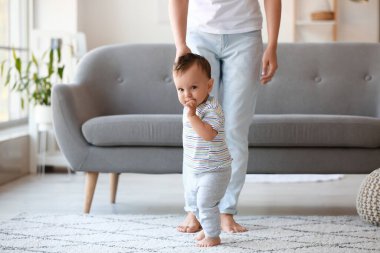 Küçük bebek annesinin yardımıyla evde yürümeyi öğreniyor.