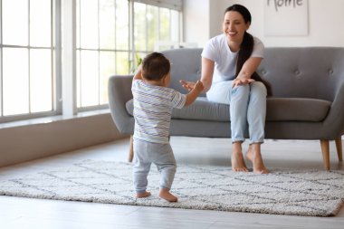 Küçük çocuk annesiyle evde yürümeyi öğreniyor.