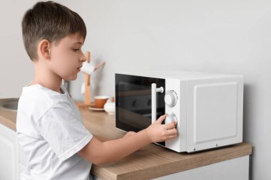 Küçük çocuk mikrodalga fırında yemek ısıtıyor.