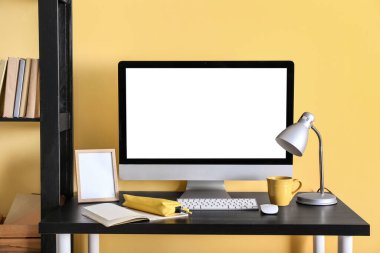 Renk duvarına yakın modern bilgisayar, defter, bardak ve lambalı işyeri