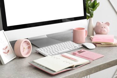 Modern bilgisayar, çalar saat, defterler ve fincanlar gri masada.