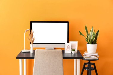 Modern bilgisayar, ev bitkisi ve renkli duvara yakın kitapları olan rahat bir iş yeri