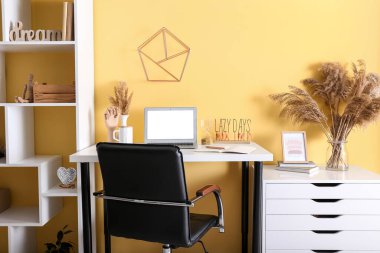 Modern işyeri, raf ünitesi ve renkli duvarın yanındaki çekmecelerin olduğu şık bir oda.