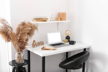 Modern dizüstü bilgisayarlı şık bir iş yeri. Odanın içinde beyaz duvarın yanında.