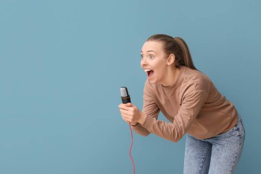 Profesyonel mikrofonlu genç bir kadın mavi arka planda şarkı söylüyor.