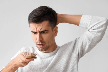 Tedirgin genç adam elinde fırça tutarken saçı açık arka planda düşmüş.