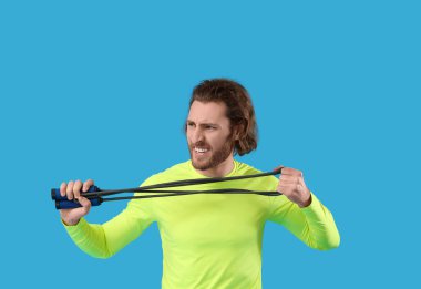 Mavi arka planda ip atlayan sportif bir adam.