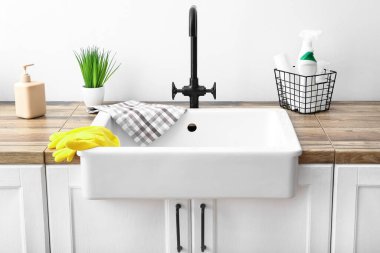 Lastik eldivenli modern lavabo ve beyaz duvarın yanındaki deterjanlı sepet.