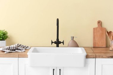 Mutfak gereçleri ve renkli duvarın yanında seramik lavabo olan tezgah.