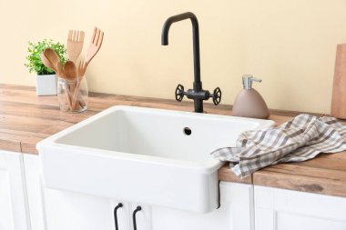 Mutfak gereçleri, havlu ve seramik lavabo renkli duvarın yanında.