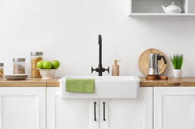 Farklı aletlerle tezgah, taze elma ve seramik lavabo, ışık duvarının yanında.