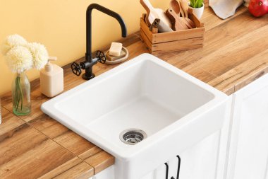 Modern lavabosu olan ahşap tezgah, farklı mutfak aletleri ve renk duvarına yakın kasımpatı çiçekleri.