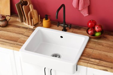 Ahşap tezgah, modern lavabo, mutfak aletleri ve renkli duvarın yanında taze meyveler.