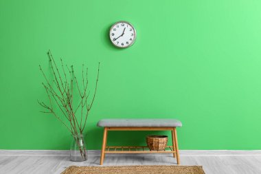 Yeşil duvarda ağaç dalları, bank ve saat asılı vazo
