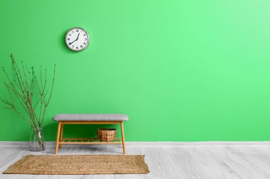 Yeşil duvarda ağaç dalları, bank ve saat asılı vazo